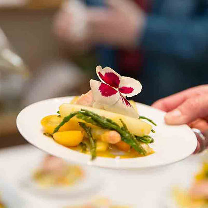 Feinkostgericht mit Gemüse und essbarer Blüte auf Teller.