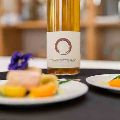 Flasche Vinaigrette Elisa, Teller mit Feinkost im Vordergrund.