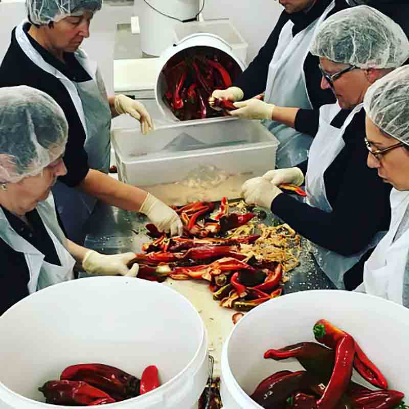 Personen verarbeiten rote Chilis in einer Produktionsumgebung.