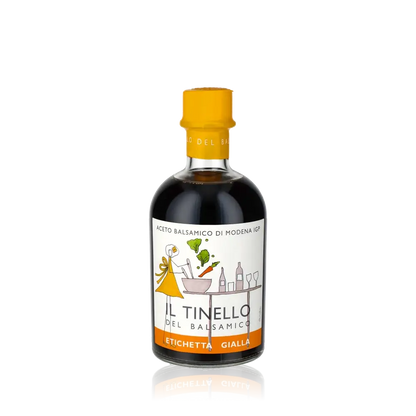 Balsamico-Essigflasche Il Tinello Gelbes Etikett vor schwarzem Hintergrund.