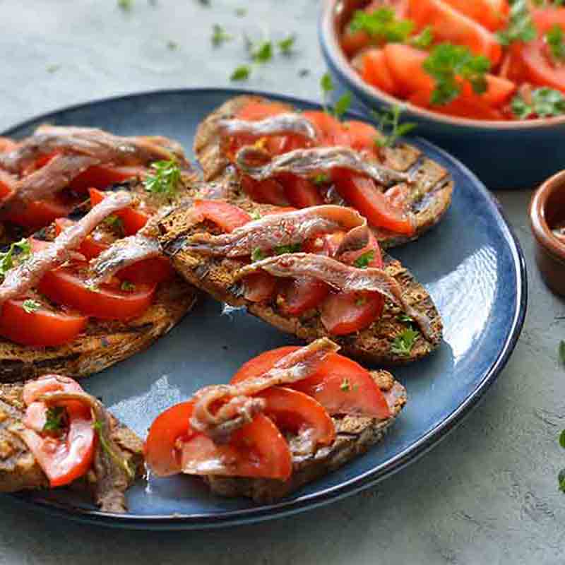 Bruschetta mit Tomaten und Sardellen auf blauem Teller.
