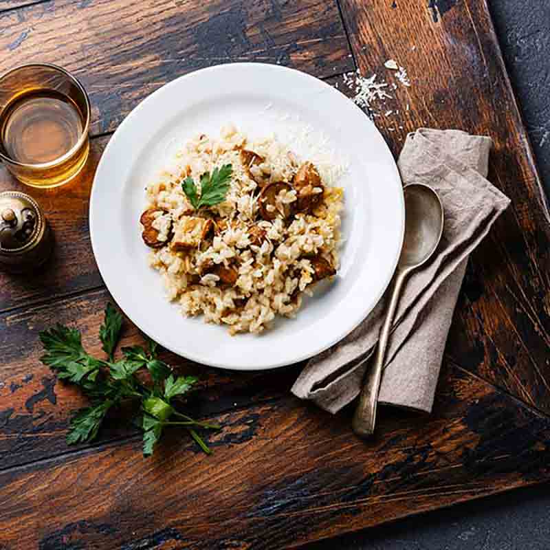 Teller mit Steinpilzrisotto, Glas Wein, Besteck, Petersilie.