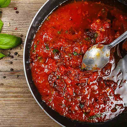 Tomatensugo in einem Topf. Daneben liegt ein Basilikum-Blatt.