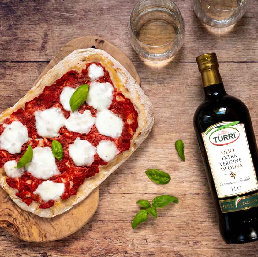 Pizza mit Turri Olivenöl und Gläsern auf Holztisch.