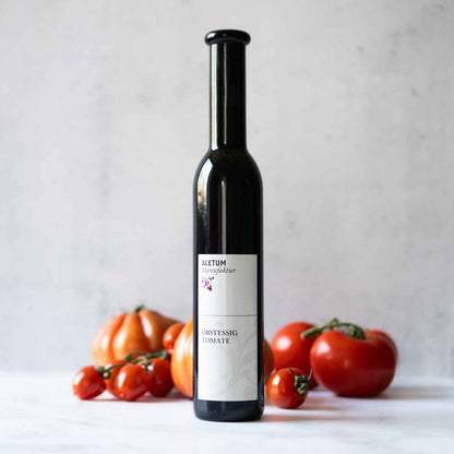 Flasche Acetum Tomatenessig vor frischen Tomaten.
