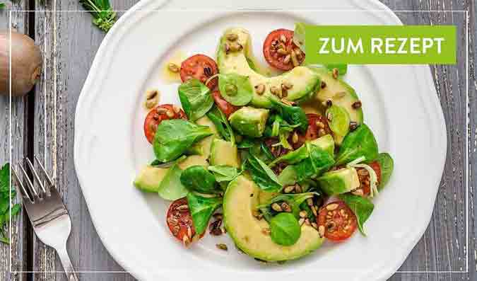 Avocado-Tomaten-Salat mit Spinat und Kernen auf Teller.