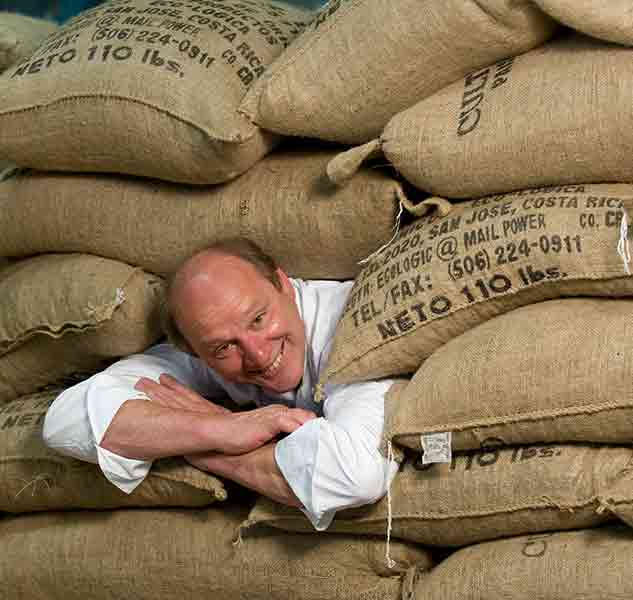 Mann zwischen Kaffeesäcken lächelnd.