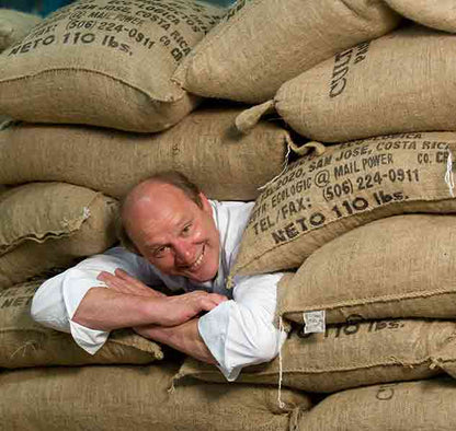 Mann zwischen Kaffeesäcken lächelnd.