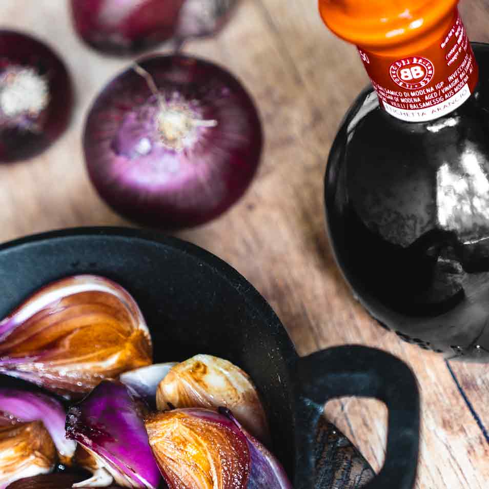 Borgo Balsamico Essigflasche, rote Zwiebeln, Holzuntergrund.