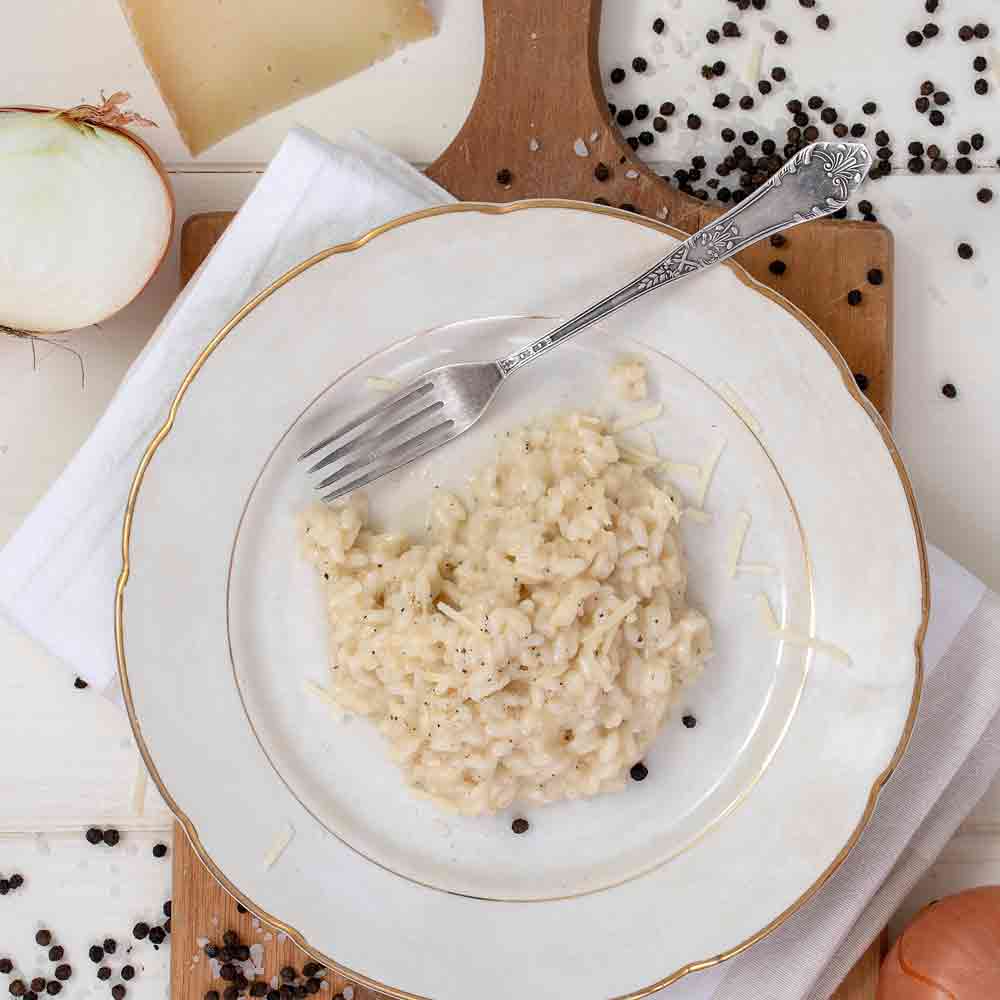 Risotto auf Teller mit Gabel, Pfefferkörner, Zwiebel, Käse.