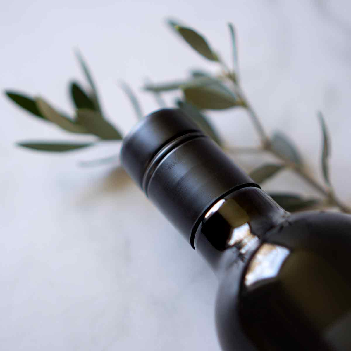 Flasche Olivenöl mit Olivenzweig auf Marmortisch.