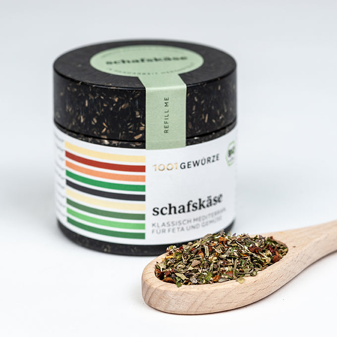Gewürzdose und Holzlöffel mit Kräutermischung für Schafskäse.