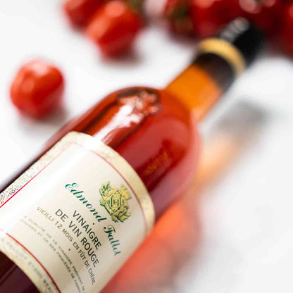 Edmond Fallot Rotweinessig Flasche mit Tomaten im Hintergrund.