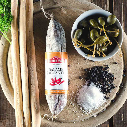 Salami, Grissini, Kapern, Salz, Pfeffer auf Holzbrett arrangiert.