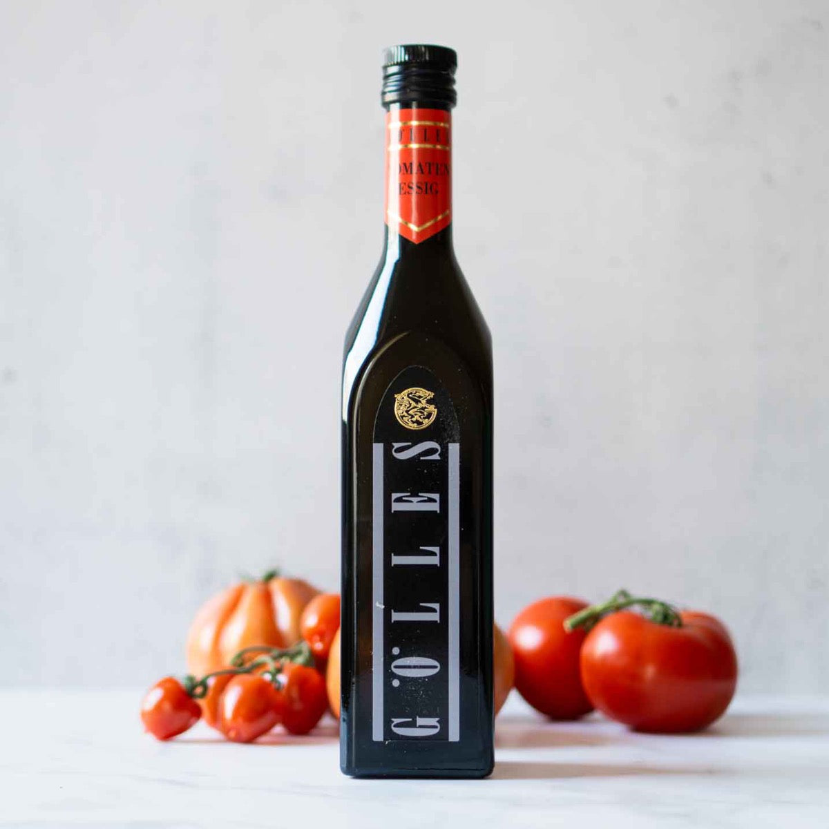 Gölles Tomatenessig Flasche vor frischen Tomaten auf Tisch.