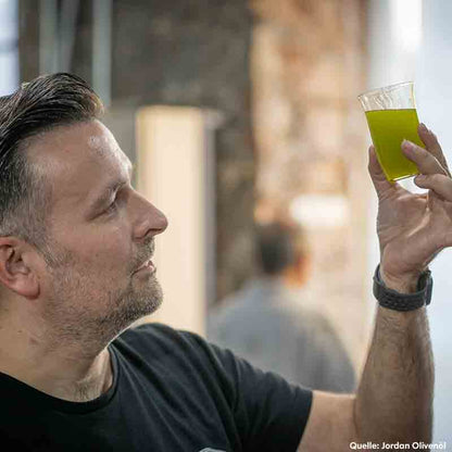 Mann betrachtet Glas mit Olivenöl.