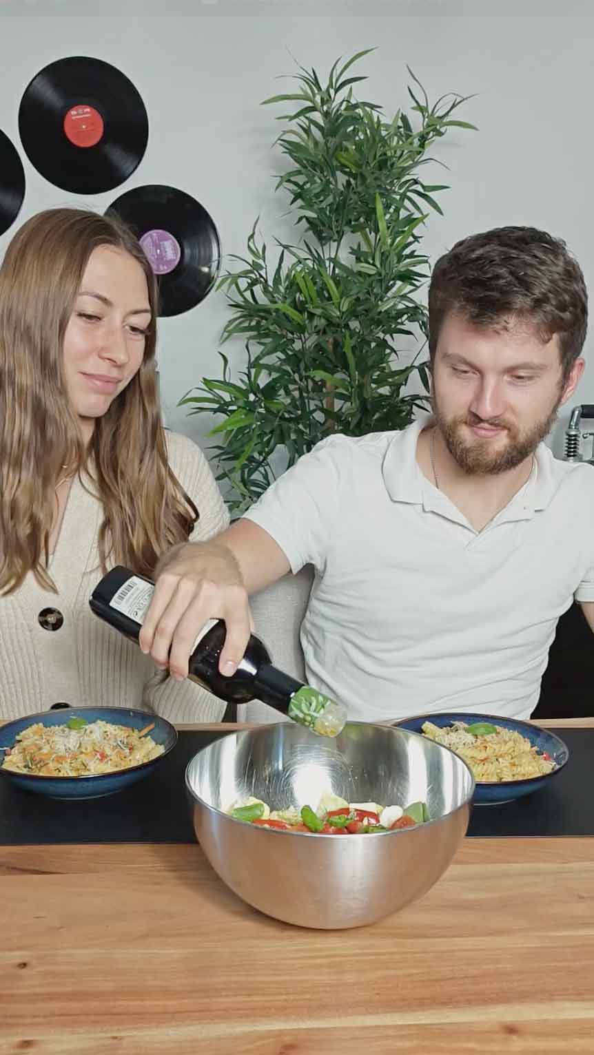 Zwei Personen geben bestes Olivenöl über einen gemischten Salat.