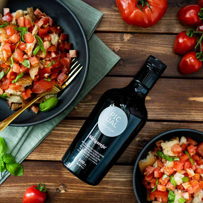 Melgarejo Olivenöl neben Panzanella-Salat und Tomaten auf Holztisch.