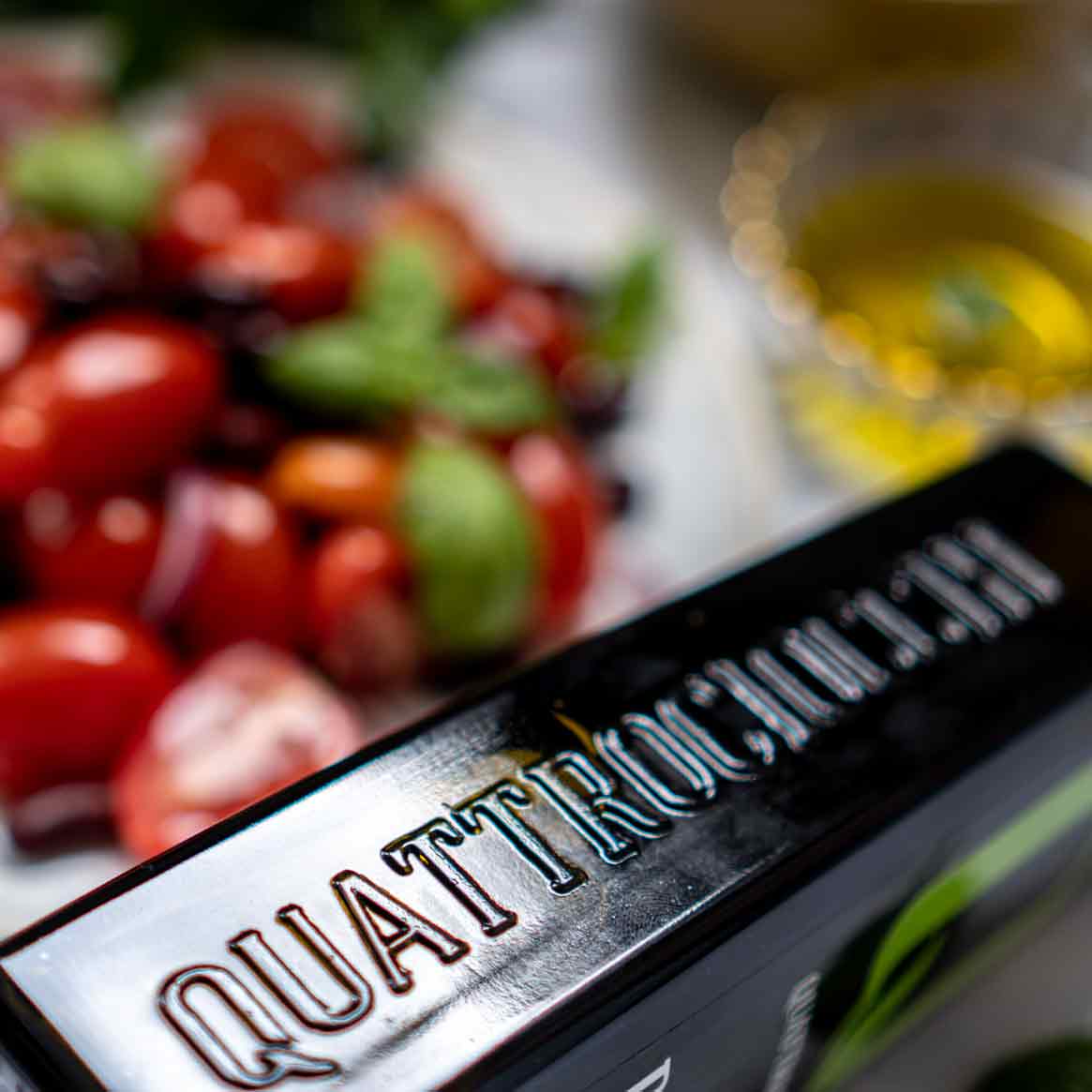 Quattrociocchi Olivenölflasche vor Tomaten und Basilikum.