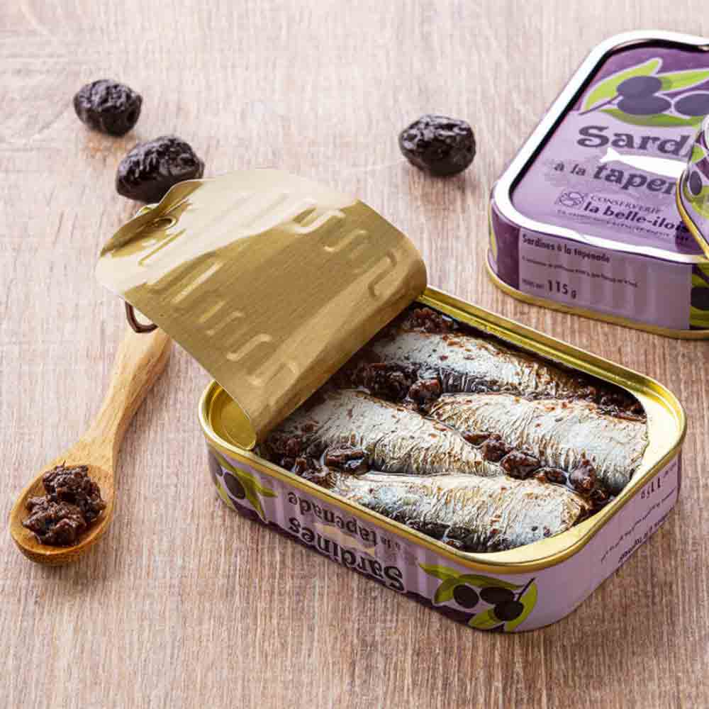Sardinen mit Oliven-Tapenade in geöffneter Dose auf Tisch.