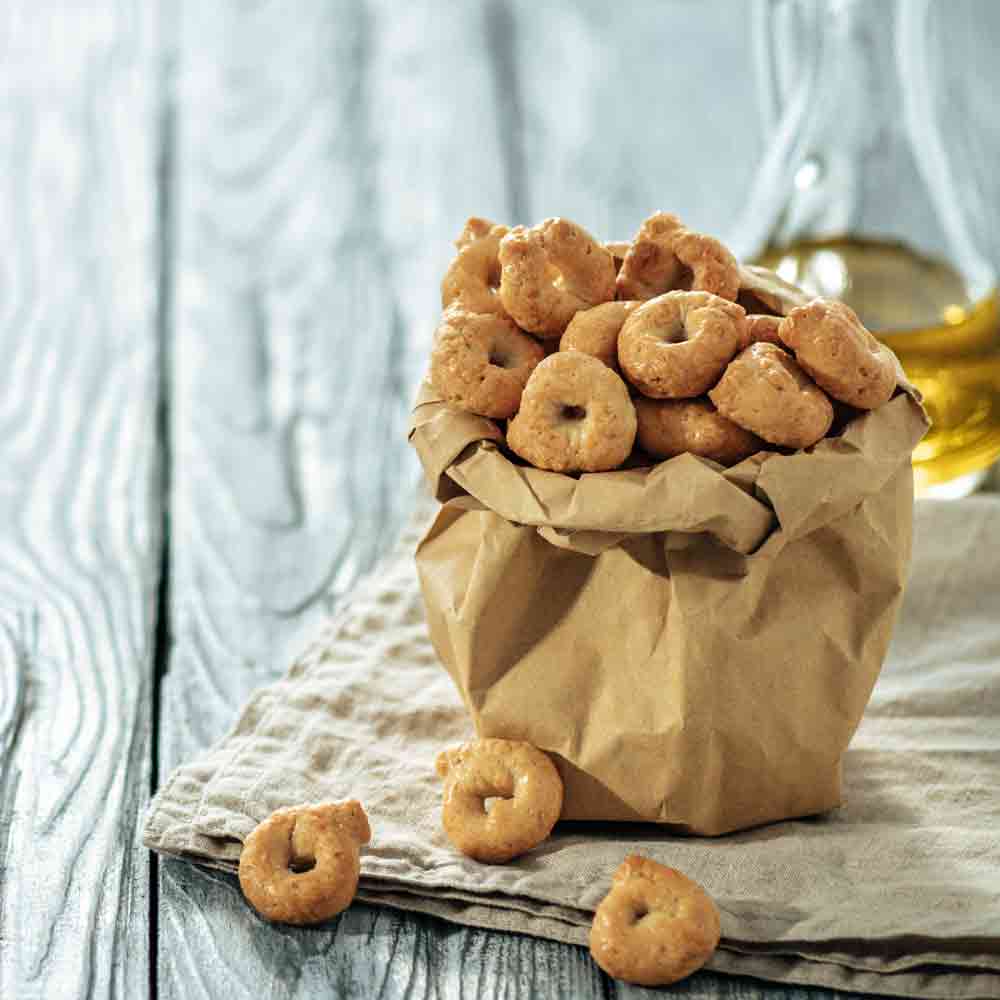 Taralli in Papiertüte, Olivenöl im Hintergrund auf Holztisch.