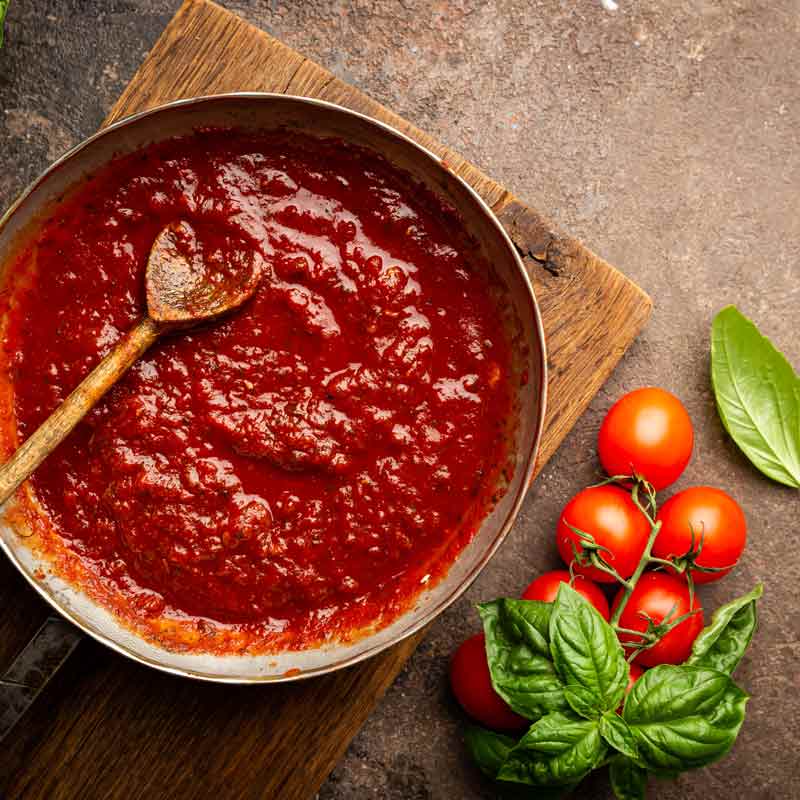Tomatensauce in Pfanne, frische Tomaten und Basilikum daneben.