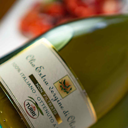 Turri Olivenölflasche vor unscharfem Hintergrund mit Tomaten.
