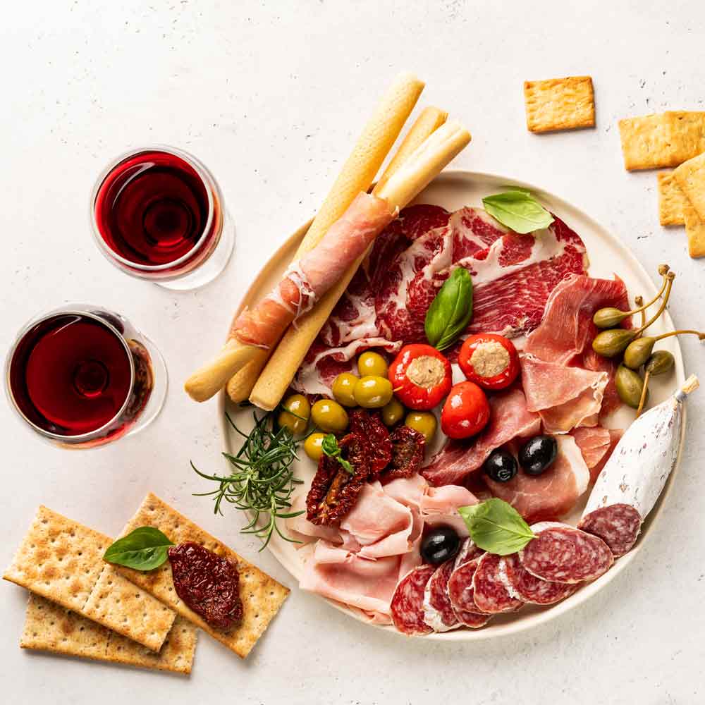 Wurstplatte mit Oliven, Brot, Wein und Kräutern auf Tisch.